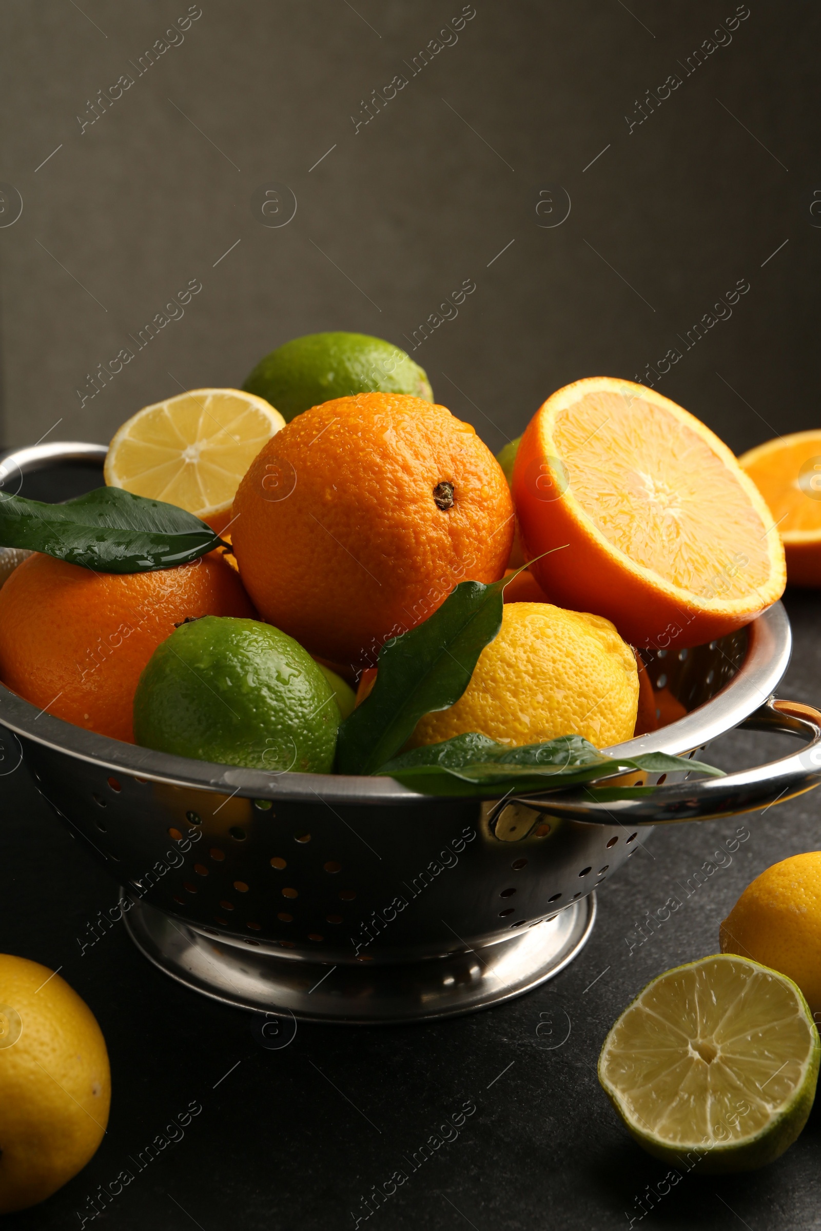 Photo of Fresh citrus fruits in colander on dark table, closeup