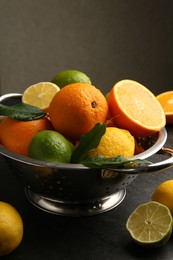 Fresh citrus fruits in colander on dark table, closeup