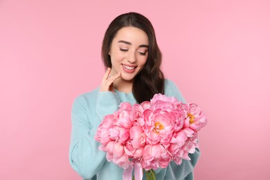 Photo of Beautiful young woman with bouquet of peonies on pink background