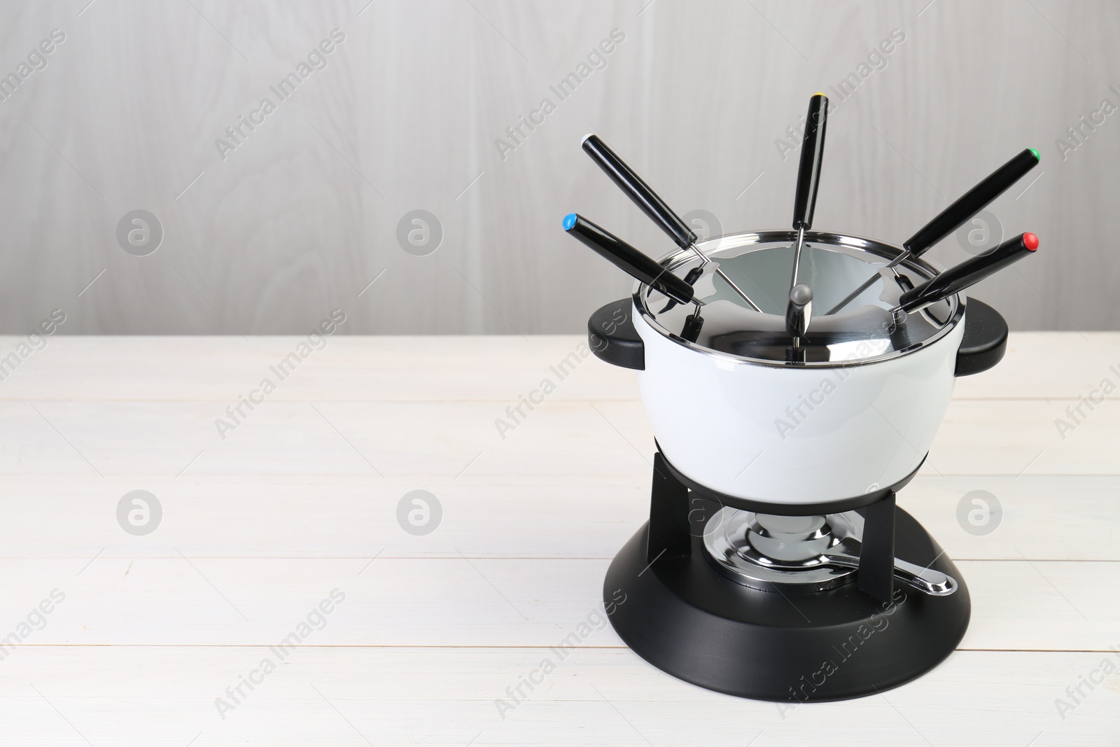 Photo of Fondue set on white wooden table, space for text