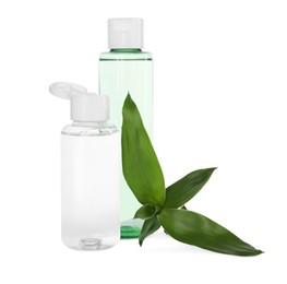 Photo of Bottles of micellar cleansing water and green plant on white background