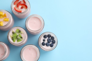 Tasty yogurt in glass jars and ingredients on light blue background, flat lay. Space for text