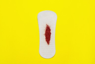 Photo of Sanitary pad with red glitter on yellow background, top view. Menstrual cycle
