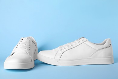 Pair of stylish white sneakers on light blue background