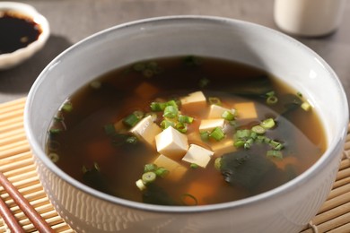 Bowl of delicious miso soup with tofu on bamboo mat, closeup