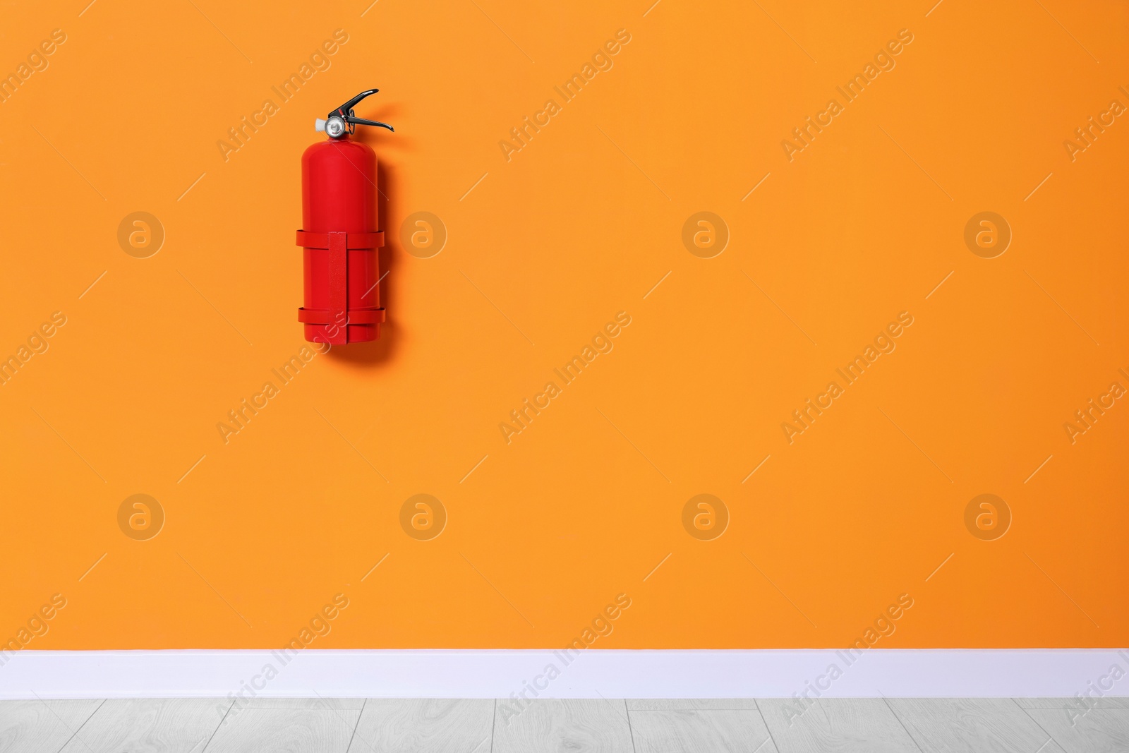 Photo of Red fire extinguisher on orange wall. Space for text