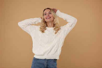 Happy woman in stylish warm sweater on beige background