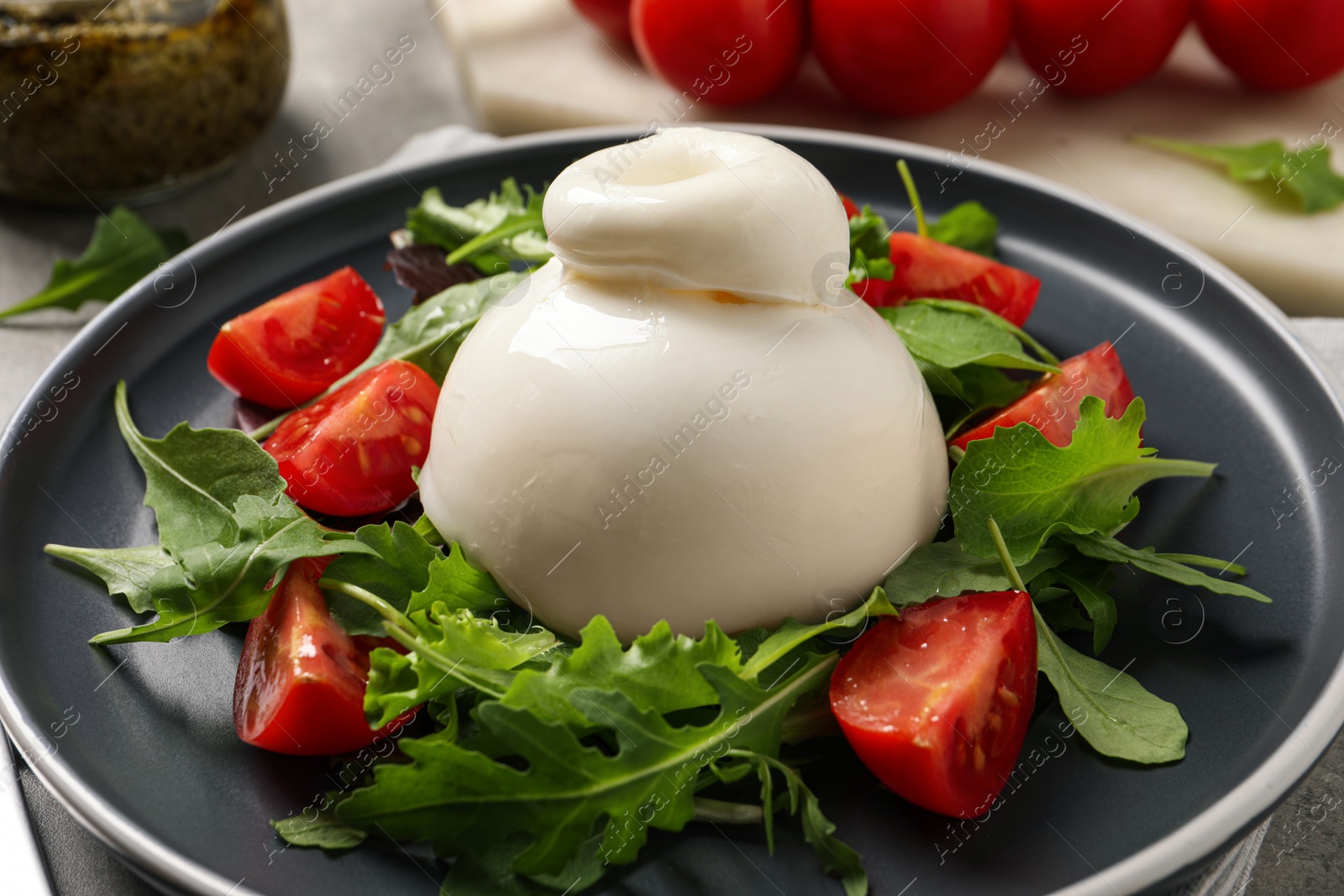 Photo of Delicious burrata salad with tomatoes and arugula on table, closeup