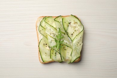 Photo of Tasty cucumber sandwich with seasoning and arugula on white wooden table, top view