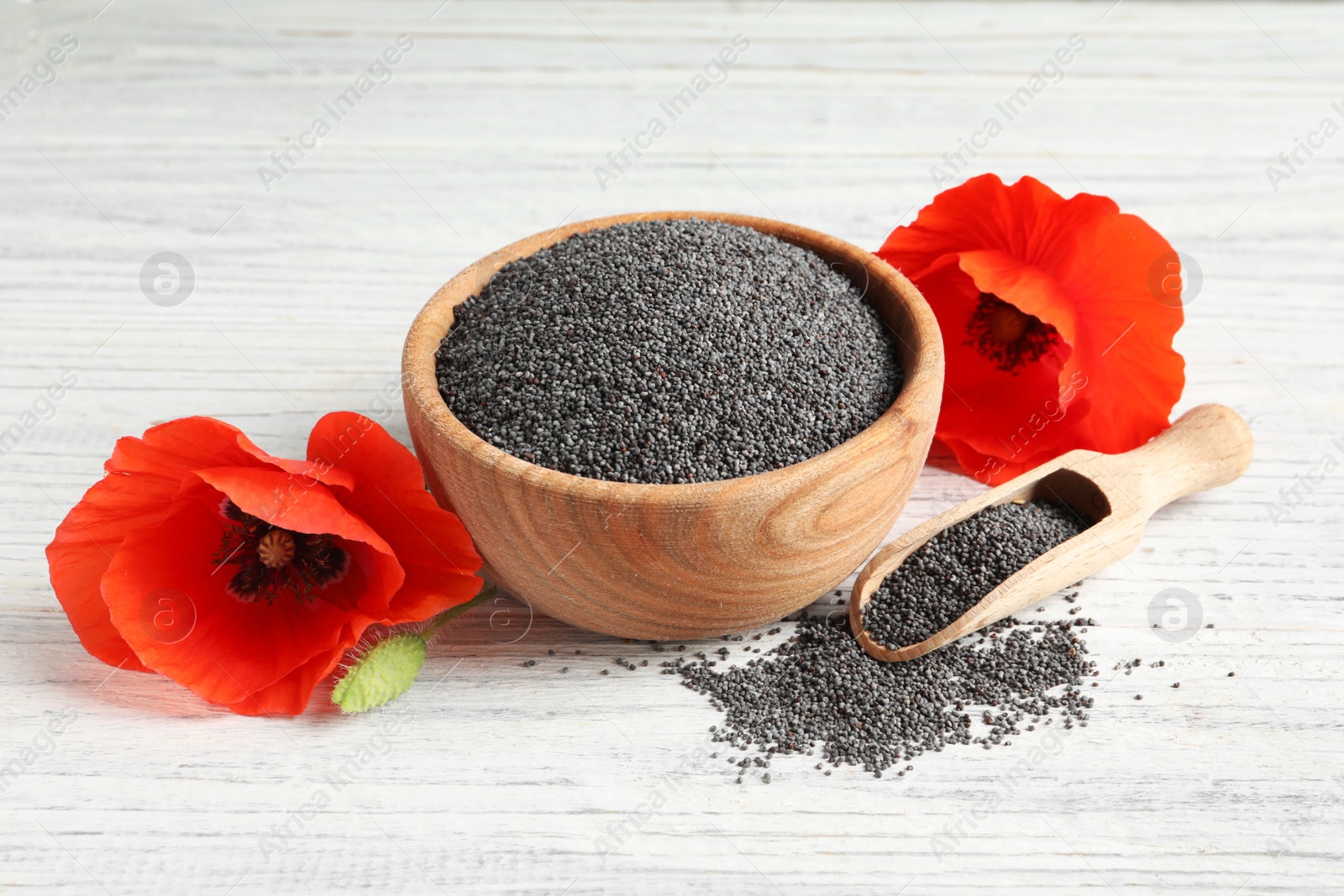 Photo of Wooden bowl of poppy seeds, scoop and flowers on white table