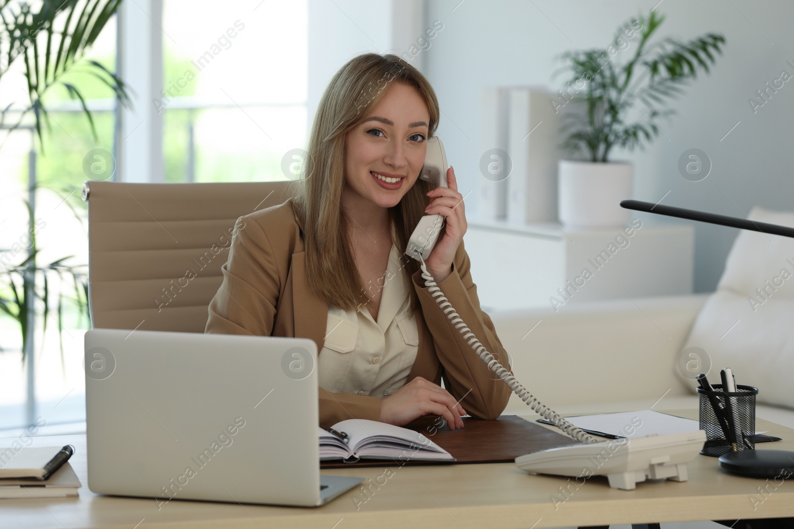 Photo of Secretary talking on phone at wooden table in office