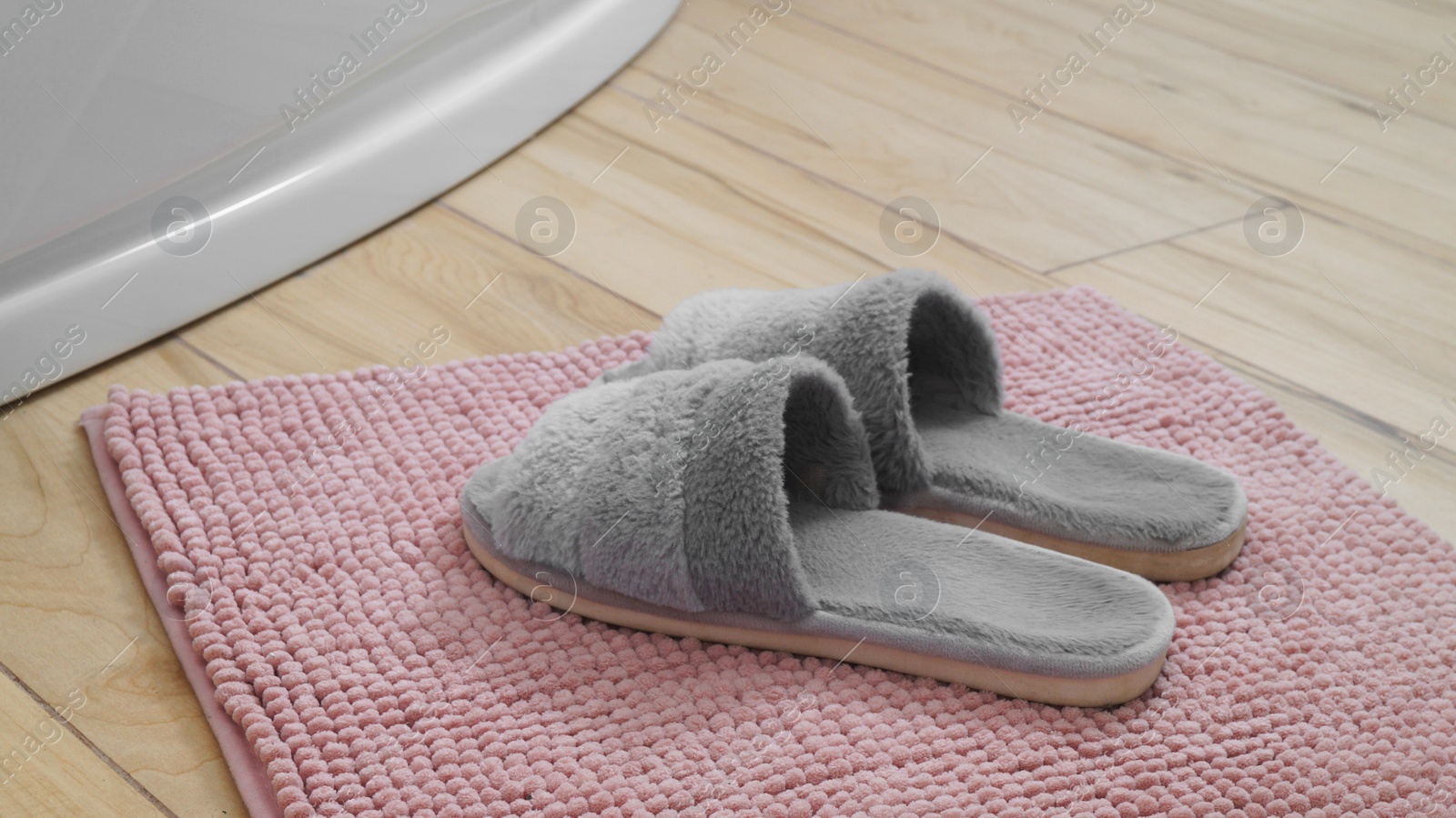 Photo of Mat with soft slippers near tub on wooden floor in bathroom