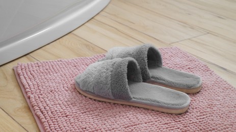 Photo of Mat with soft slippers near tub on wooden floor in bathroom