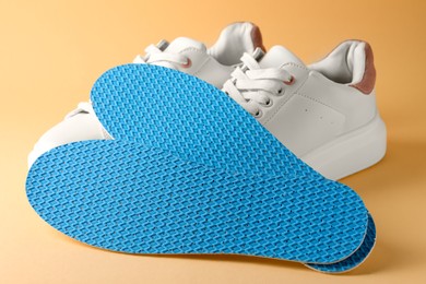 Pair of insoles and shoes on pale orange background