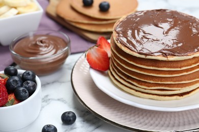 Photo of Tasty pancakes with chocolate paste and berries on white marble table, closeup