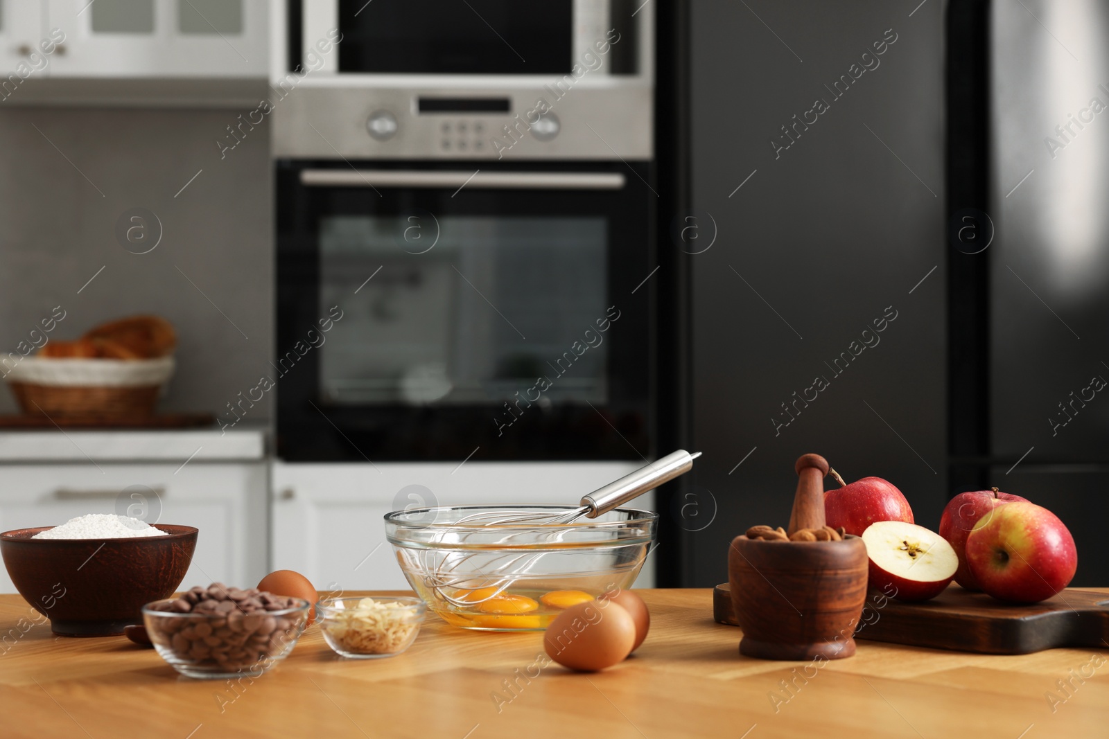 Photo of Cooking process. Metal whisk, bowl and products on wooden table in kitchen