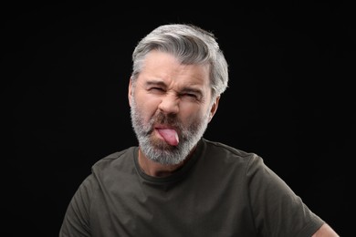 Photo of Personality concept. Bearded man showing tongue on black background