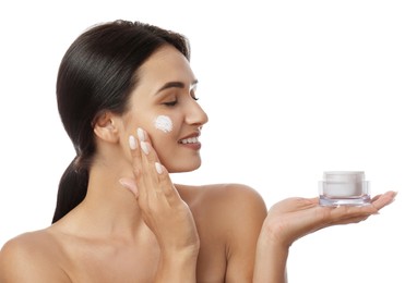 Young woman applying facial cream on white background