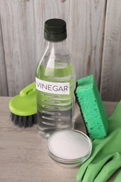 Photo of Natural cleaning products. Vinegar in bottle, baking soda, glove, sponge and brush on light wooden table