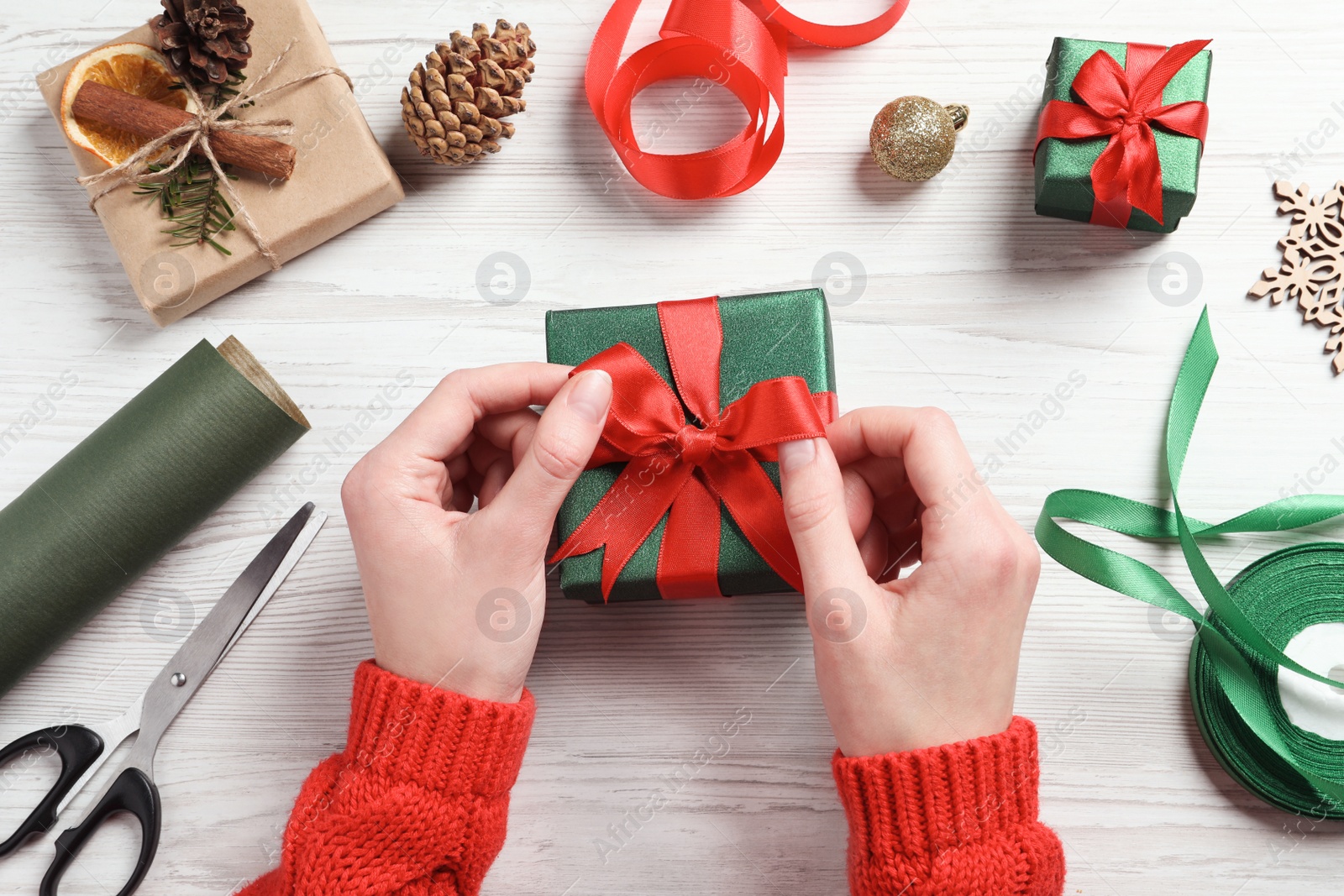 Photo of Christmas present. Woman tying ribbon bow on gift box at white wooden table, top view