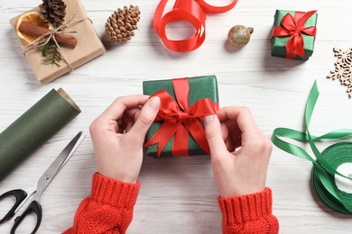 Christmas present. Woman tying ribbon bow on gift box at white wooden table, top view