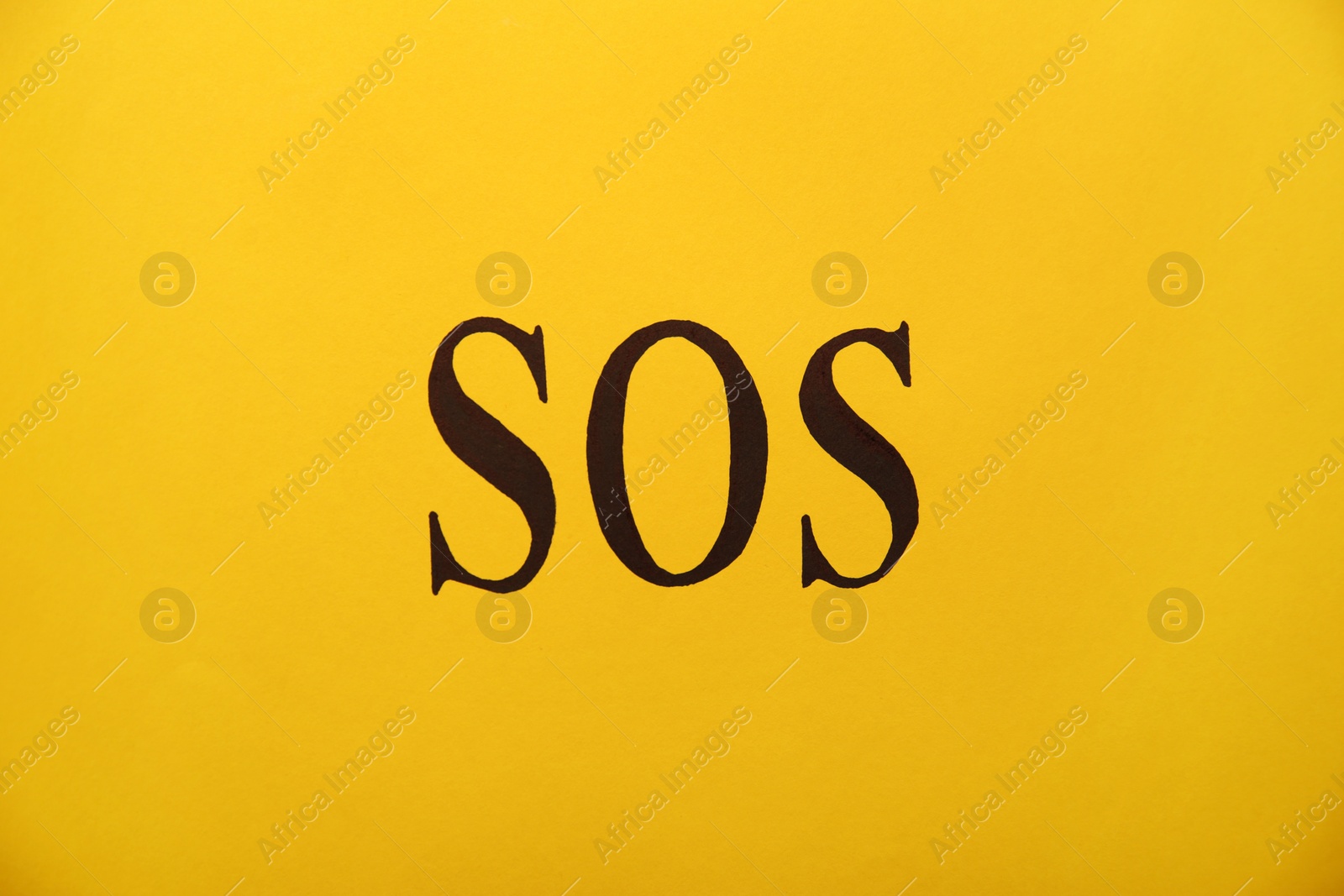 Photo of Abbreviation SOS (Save Our Souls) written on yellow background, top view