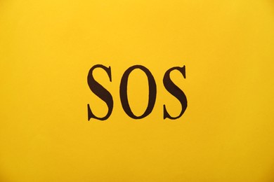 Photo of Abbreviation SOS (Save Our Souls) written on yellow background, top view
