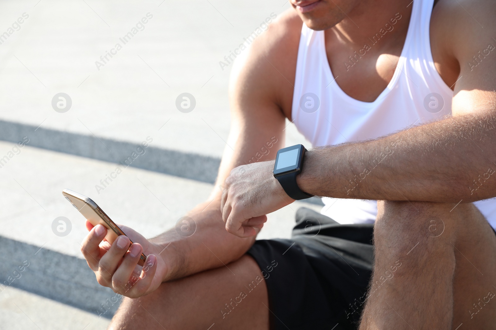 Photo of Man with fitness tracker and smartphone after training outdoors, closeup