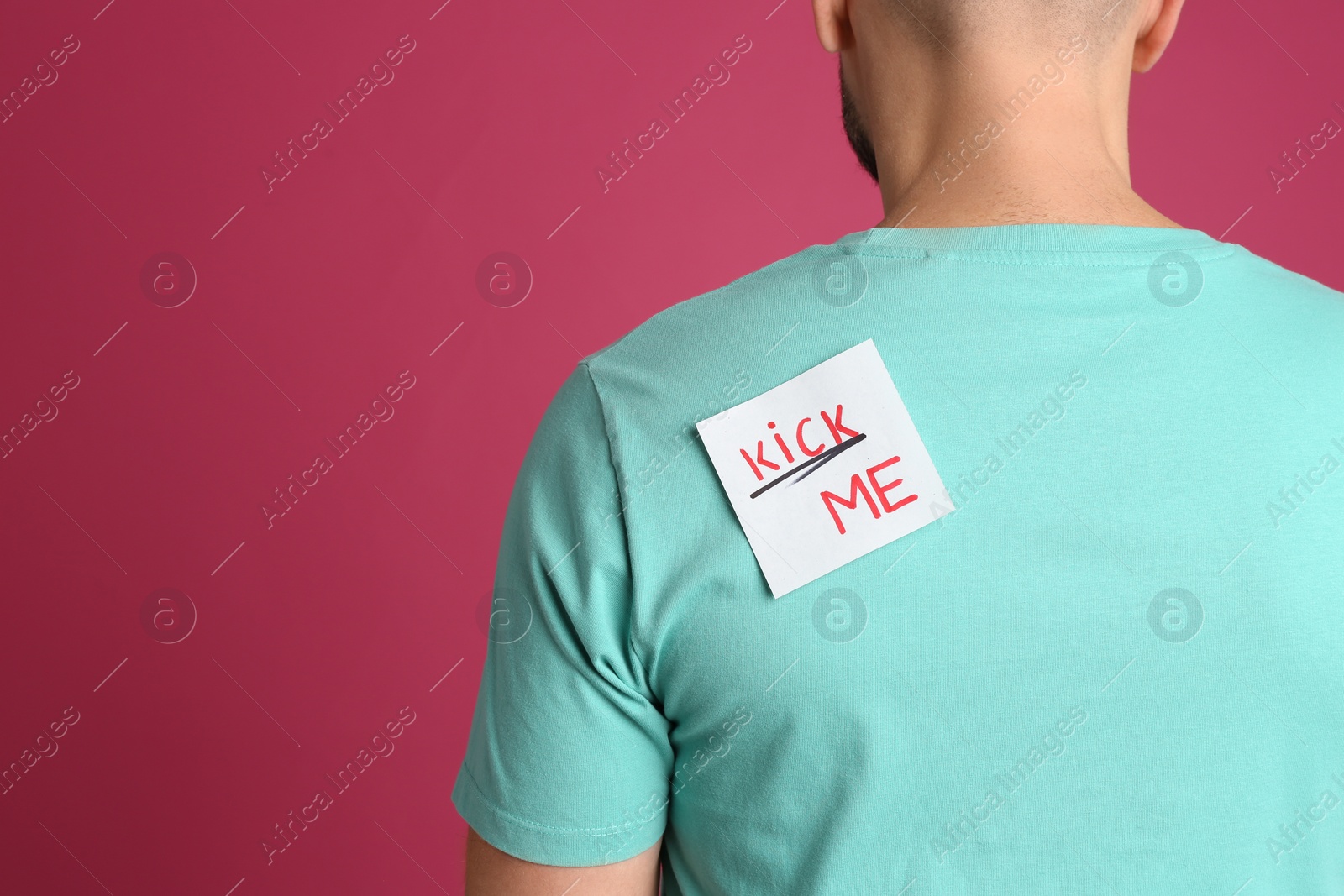 Photo of Man with KICK ME sticker on back against pink background, space for text. April fool's day