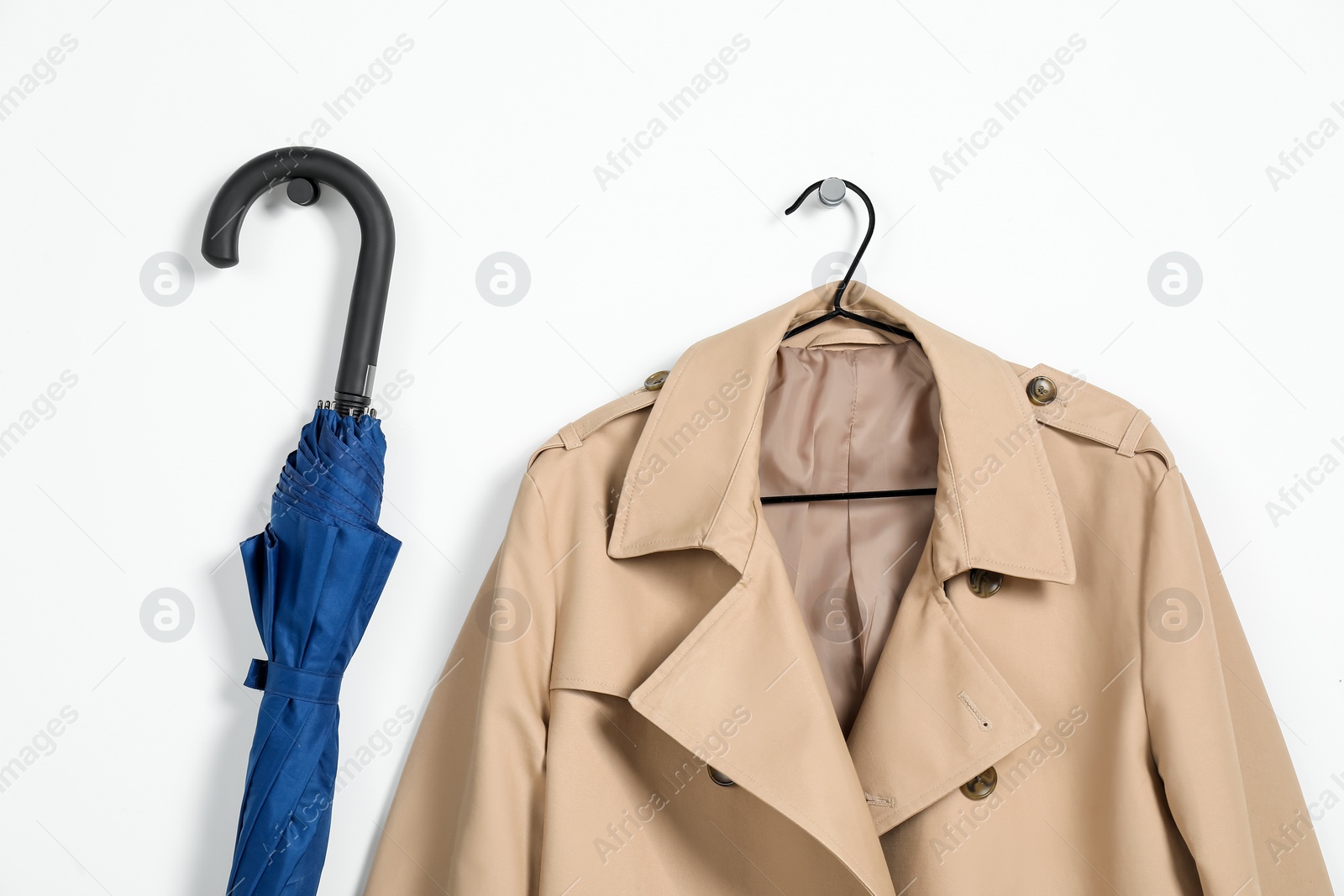 Photo of Hanger with beige trench coat and blue umbrella on white wall