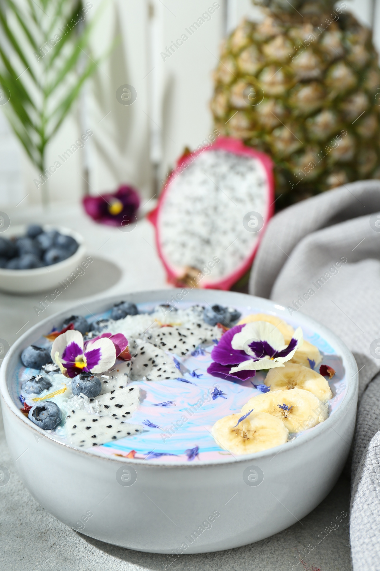 Photo of Delicious smoothie bowl with fresh fruits, blueberries and flowers on light grey table, closeup