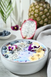 Delicious smoothie bowl with fresh fruits, blueberries and flowers on light grey table, closeup