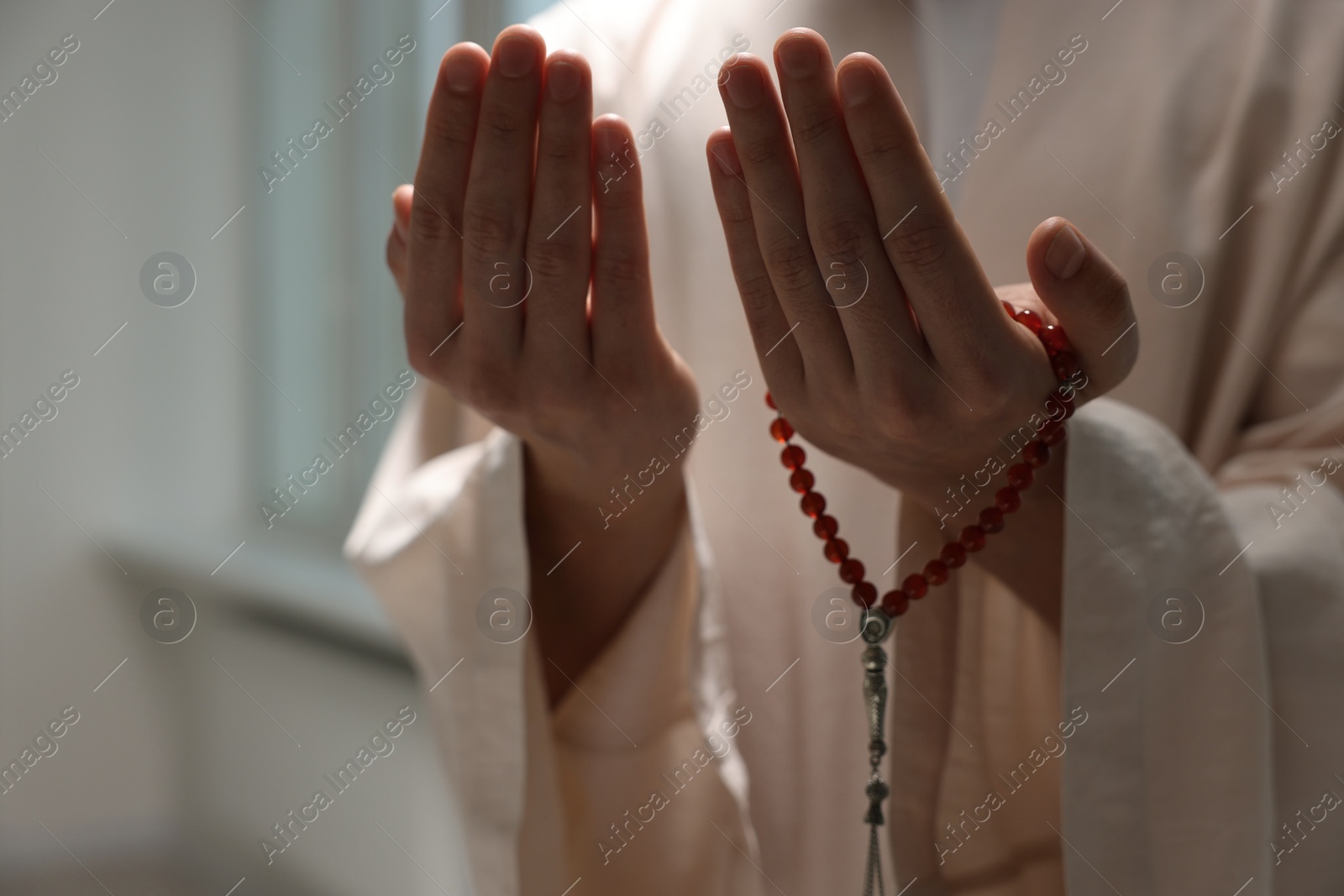 Photo of Muslim man with misbaha praying near window indoors, closeup. Space for text