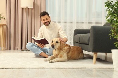 Photo of Man reading book on floor near his cute Labrador Retriever at home