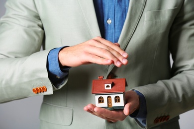 Male agent covering house model, closeup. Home insurance