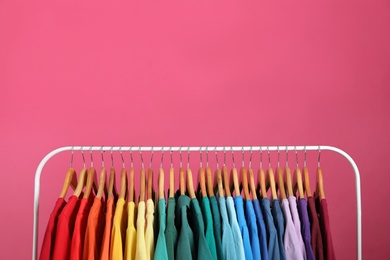 Photo of Rack with bright clothes on pink background, space for text. Rainbow colors