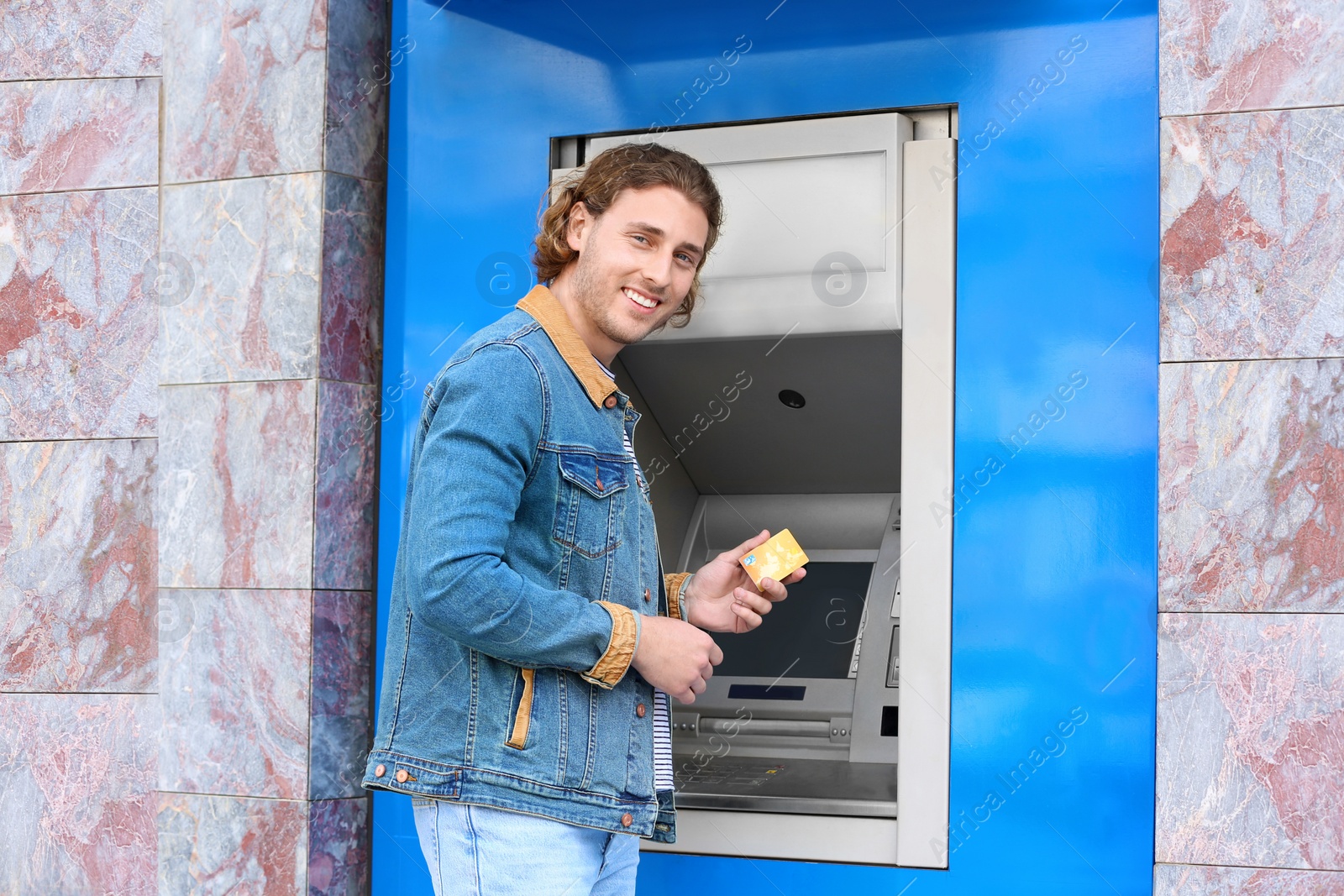 Photo of Young man with credit card near cash machine outdoors