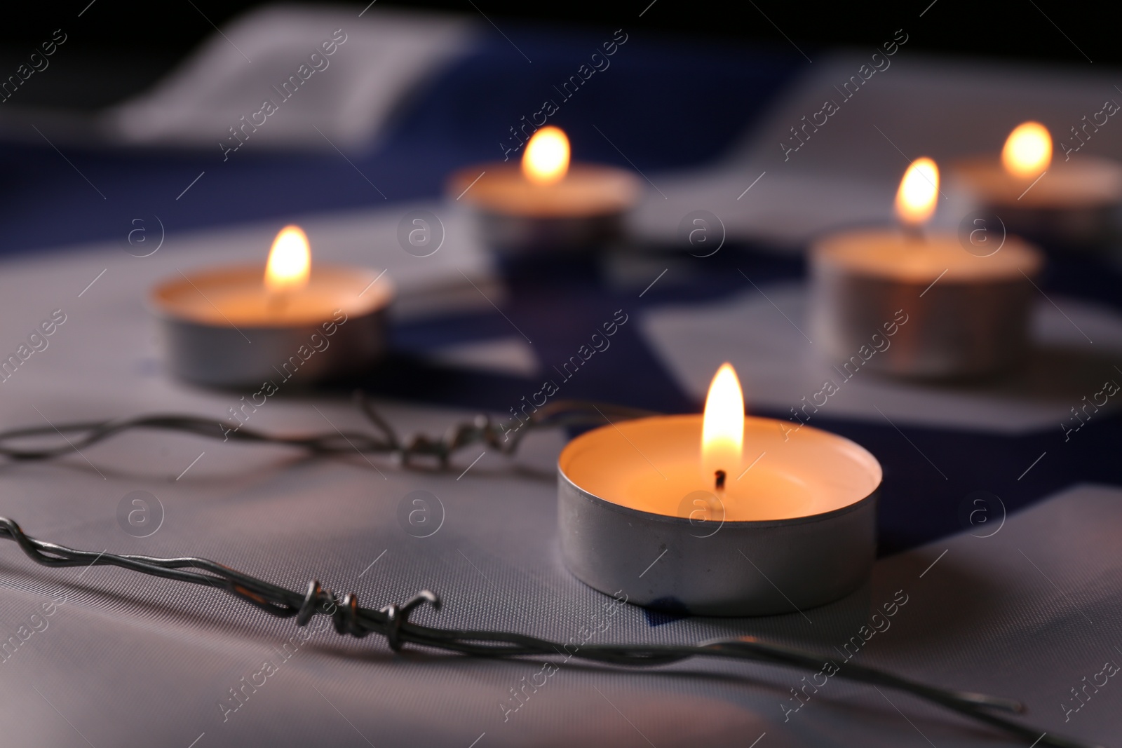 Photo of Burning candles and barbed wire on flag of Israel. Holocaust memory day