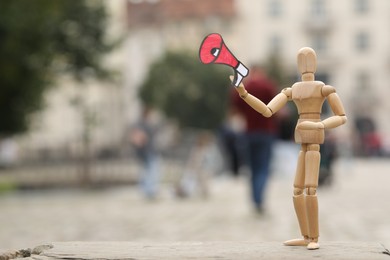 Photo of Wooden human figure with paper megaphone on city street, space for text