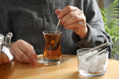 Woman stirring sugar in tea at wooden table, closeup