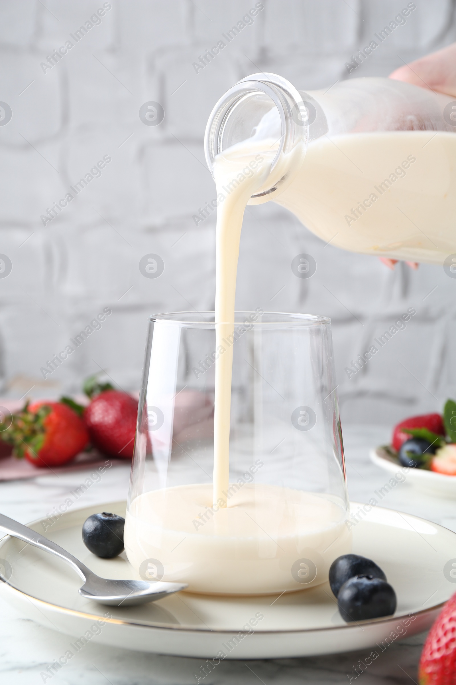 Photo of Woman pouring tasty yogurt into glass at white marble table, closeup