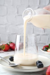 Woman pouring tasty yogurt into glass at white marble table, closeup