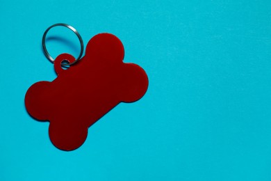 Photo of Red pet tag in shape of bone with ring on light blue background, top view. Space for text
