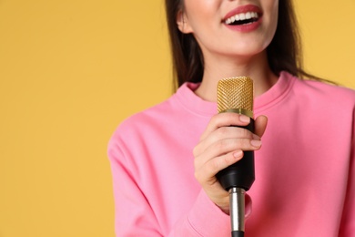 Young woman singing in microphone on color background, closeup view with space for text