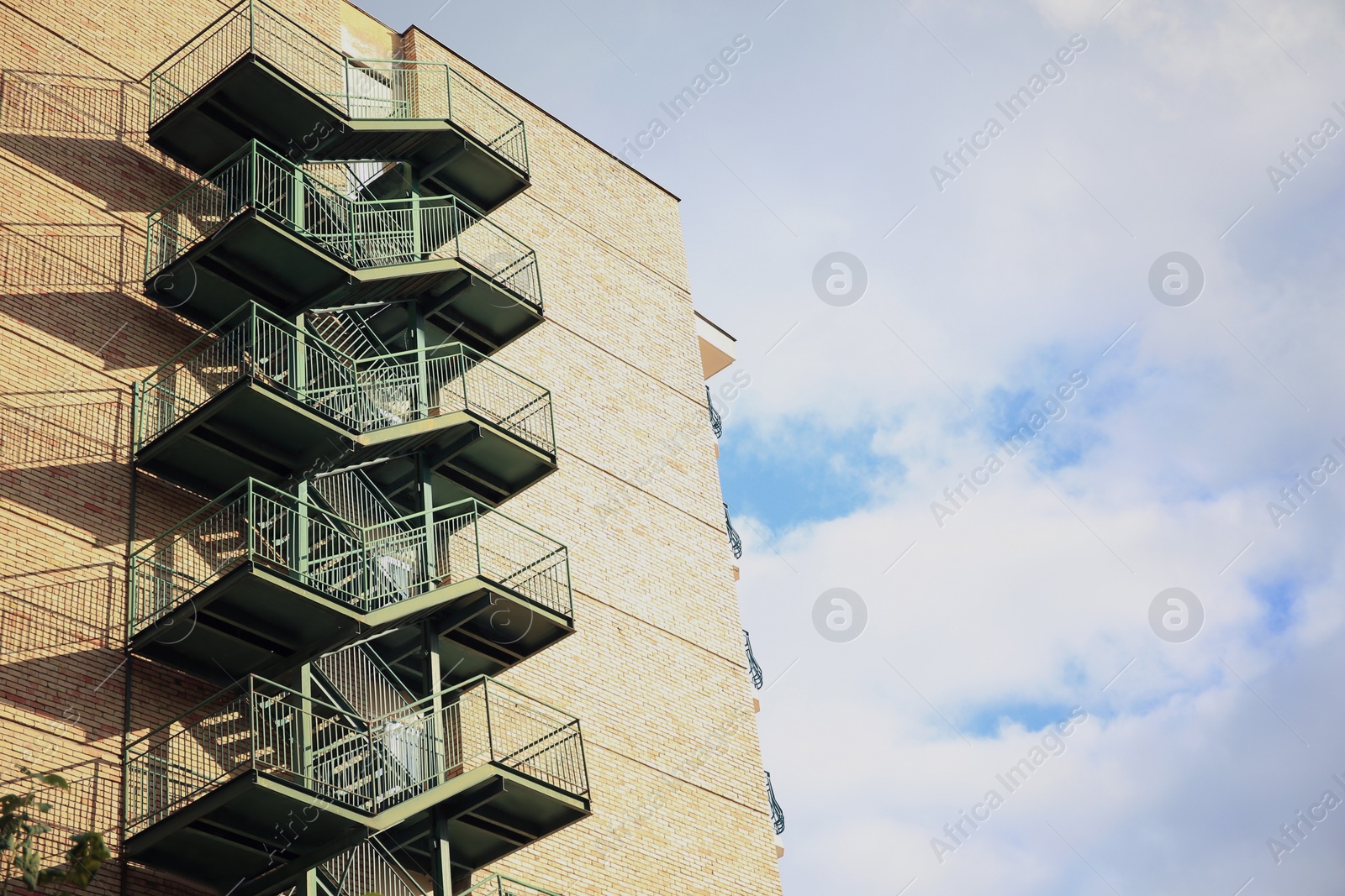 Photo of View of modern metal empty fire escape ladder near building on sunny day outdoors, space for text