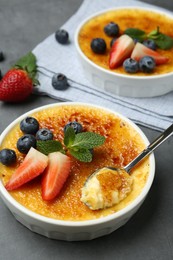 Delicious creme brulee with berries in bowl and spoon on grey table, closeup