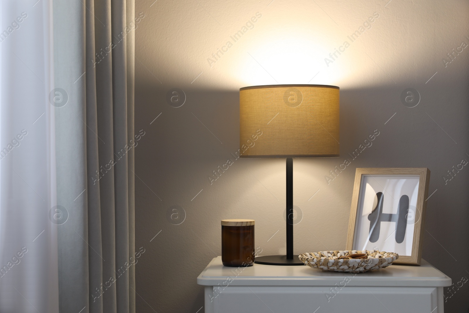 Photo of Stylish lamp and decor on white nightstand in room