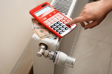 Photo of Man using calculator to count heating expenses on radiator indoors