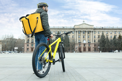 Photo of Courier with thermo bag and bicycle on city street. Food delivery service