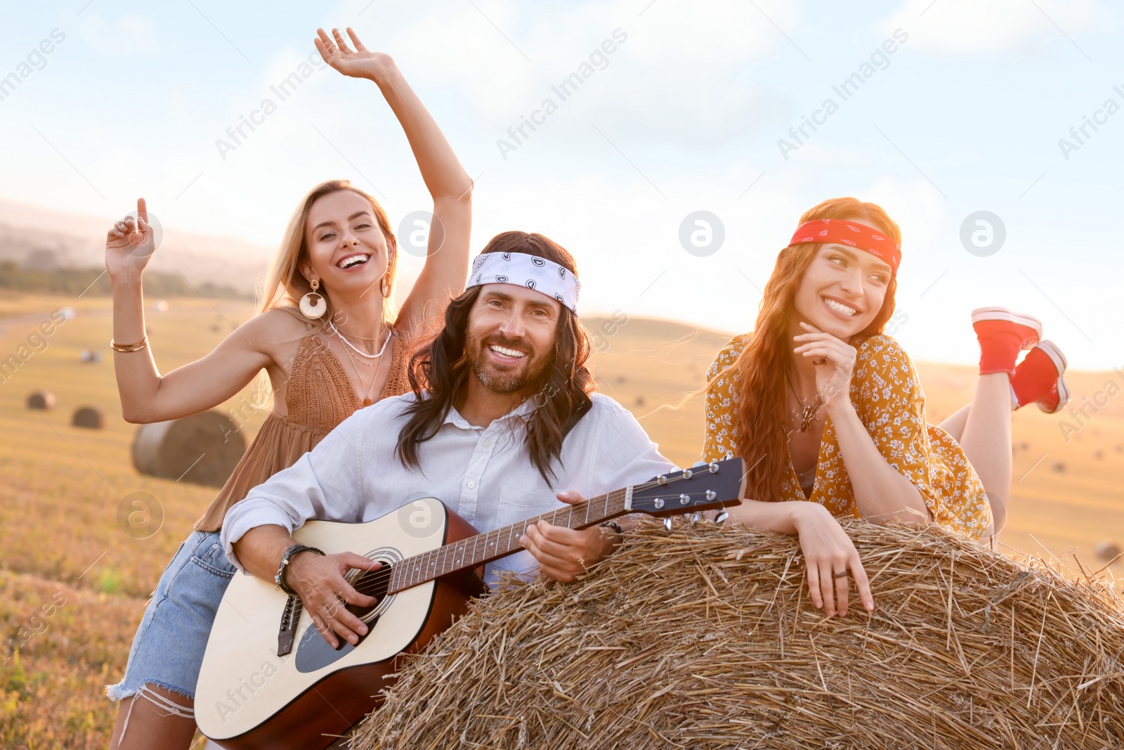 Photo of Beautiful hippie women listening to their friend playing guitar in field